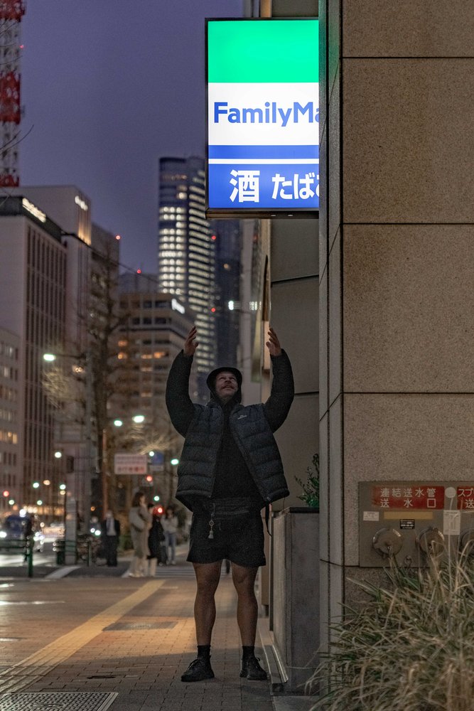 Hugh raising arms in celebration under a FamilyMart sign at night, Tokyo — Zen Den Studios