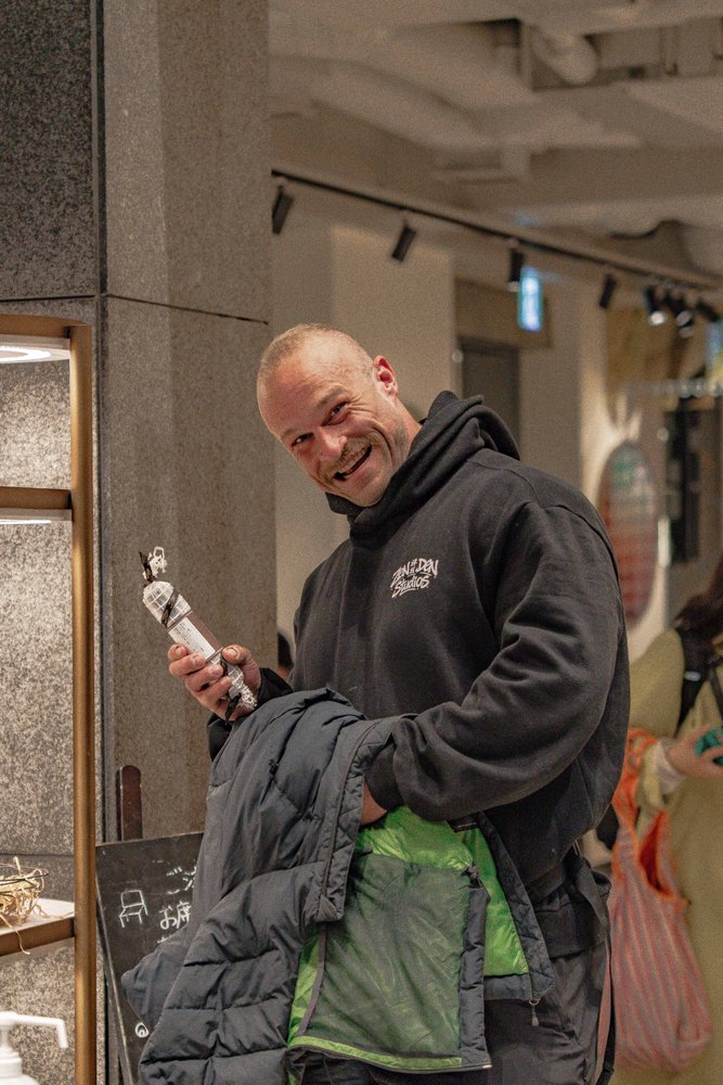 Hugh in a Zen Den Studios hoodie smiling and holding a novelty microphone figurine outside a Tokyo shop — Zen Den Studios