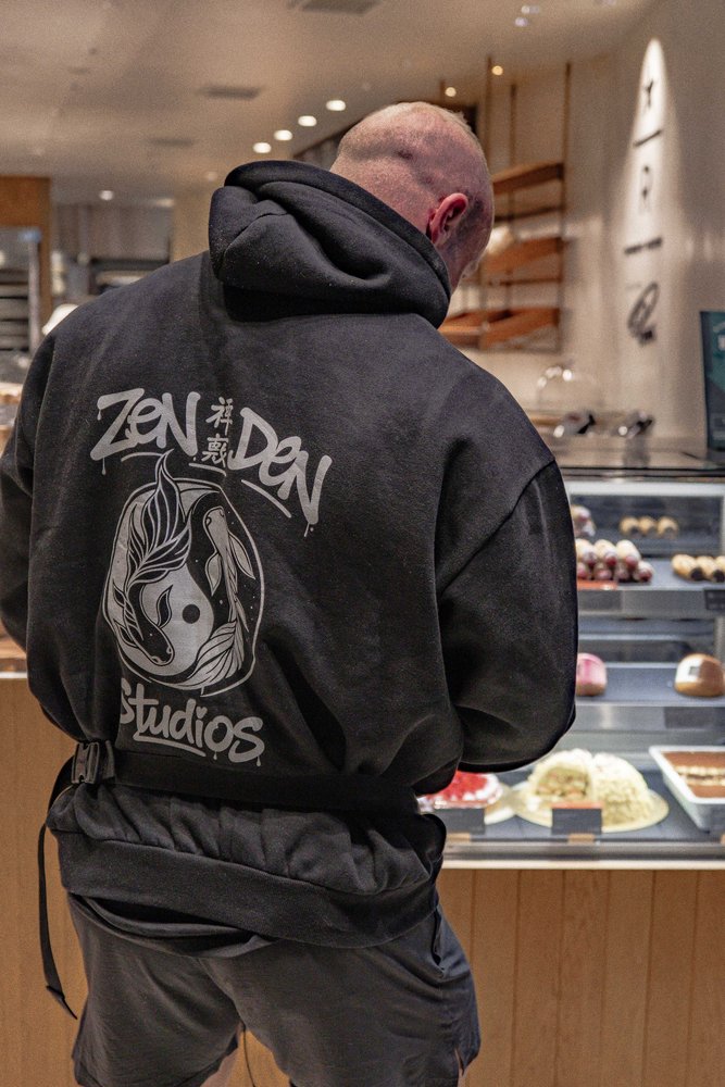 Hugh from behind in a Zen Den Studios hoodie browsing at a Tokyo patisserie display counter — Zen Den Studios