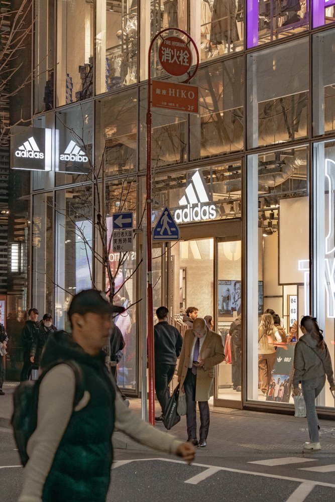 Adidas store frontage on a busy Tokyo street at night with pedestrians crossing — Zen Den Studios