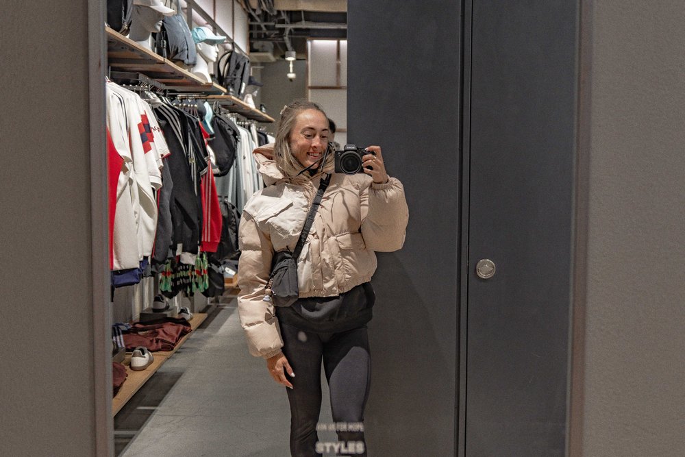 Liz smiling while taking a mirror selfie in a Tokyo clothing store — Zen Den Studios