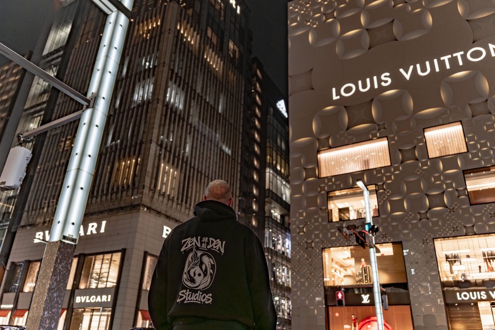 Hugh in a Zen Den Studios hoodie facing away toward the Louis Vuitton store in Ginza at night — Zen Den Studios