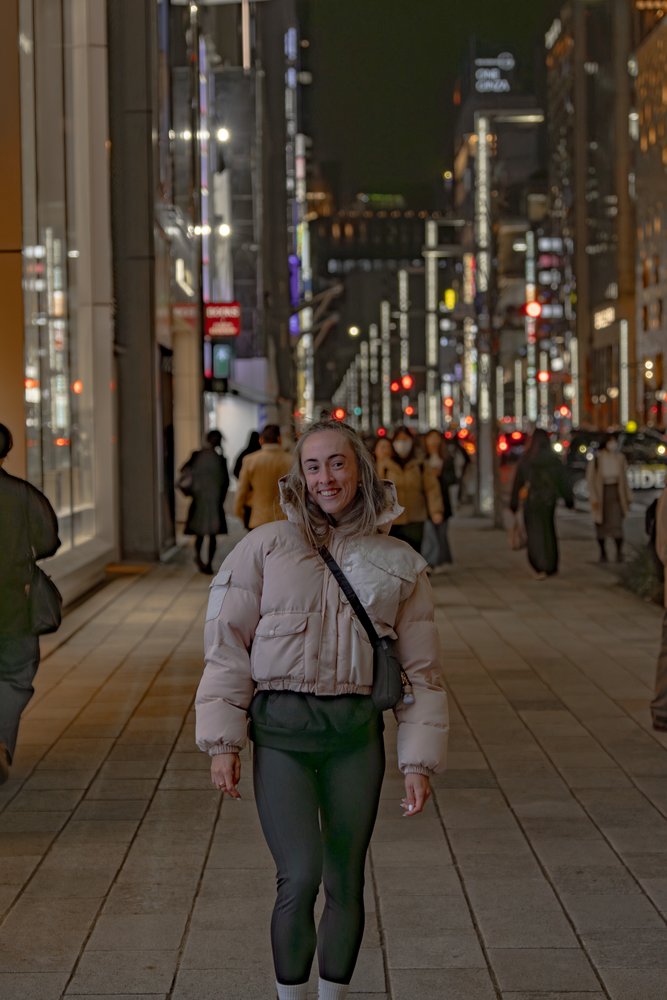 Liz smiling on a busy Ginza street at night with neon lights and crowds stretching into the distance — Zen Den Studios