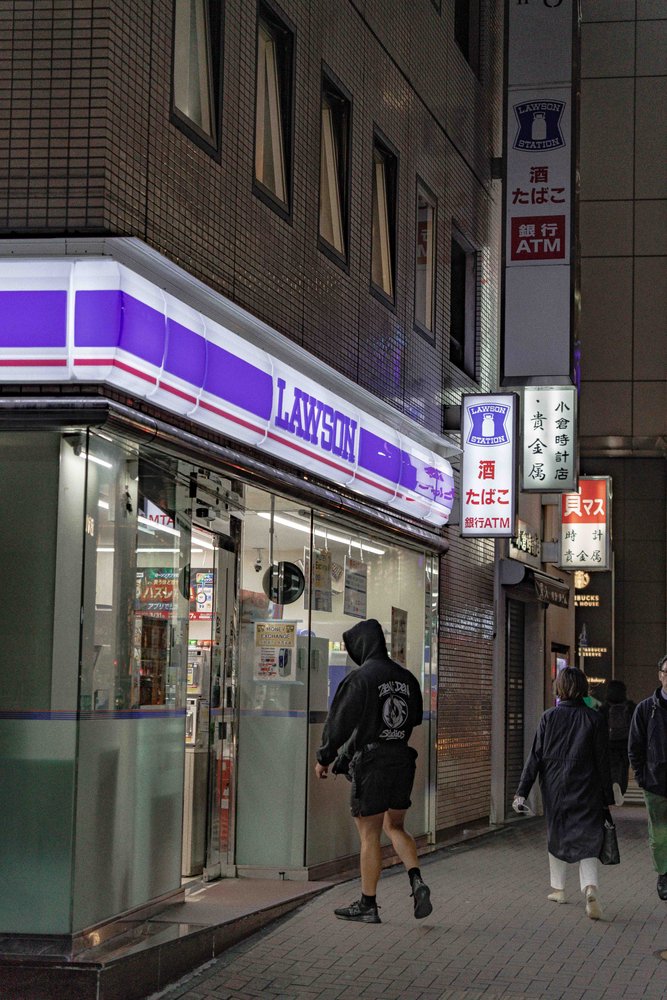 Hugh walking past a Lawson convenience store on a Tokyo street at night — Zen Den Studios